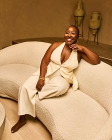 Nubia Younge smiling on a modern cream sofa, wearing a cream outfit